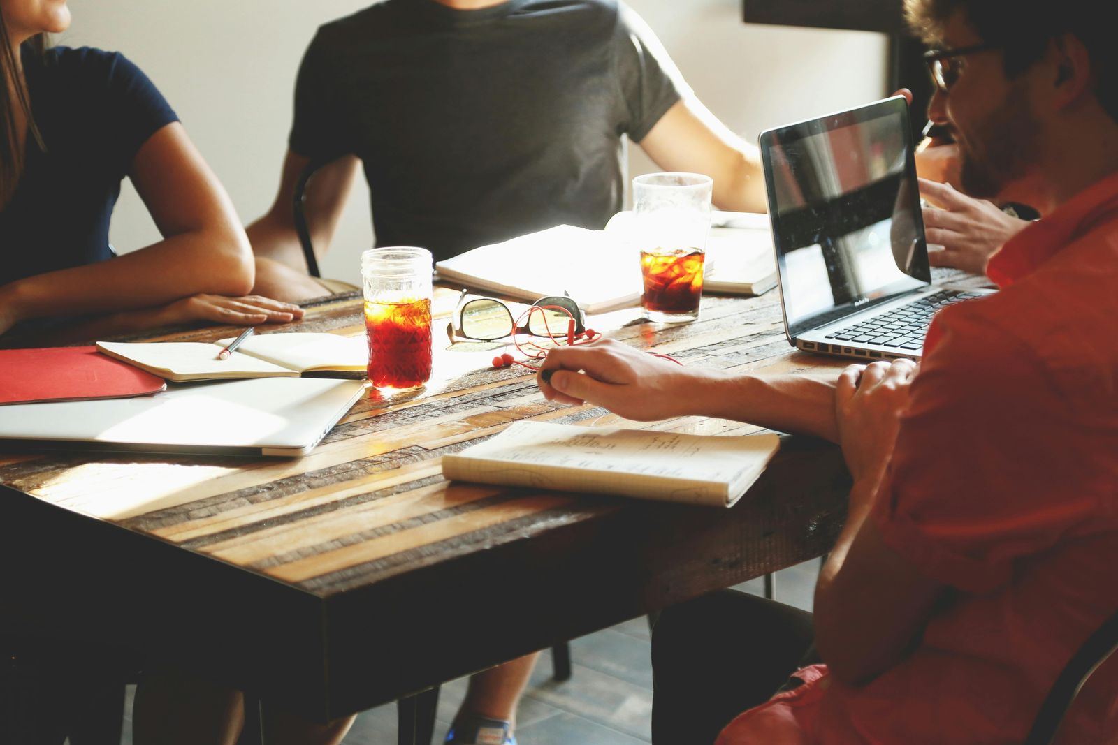 A small team discussing a project around a wooden table with a laptop and notebooks