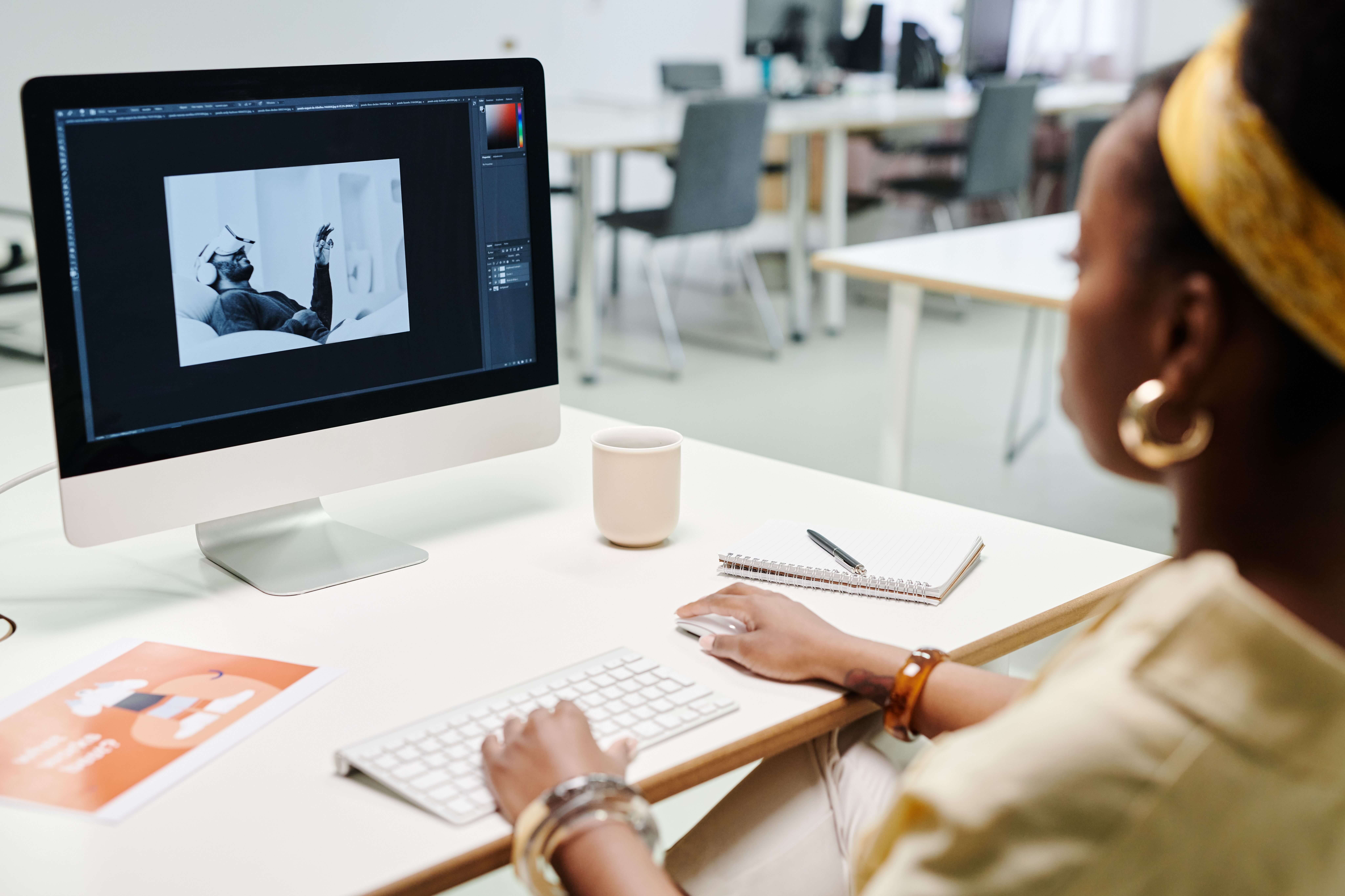 A designer editing an image in photo-editing software on a desktop computer at a studio desk