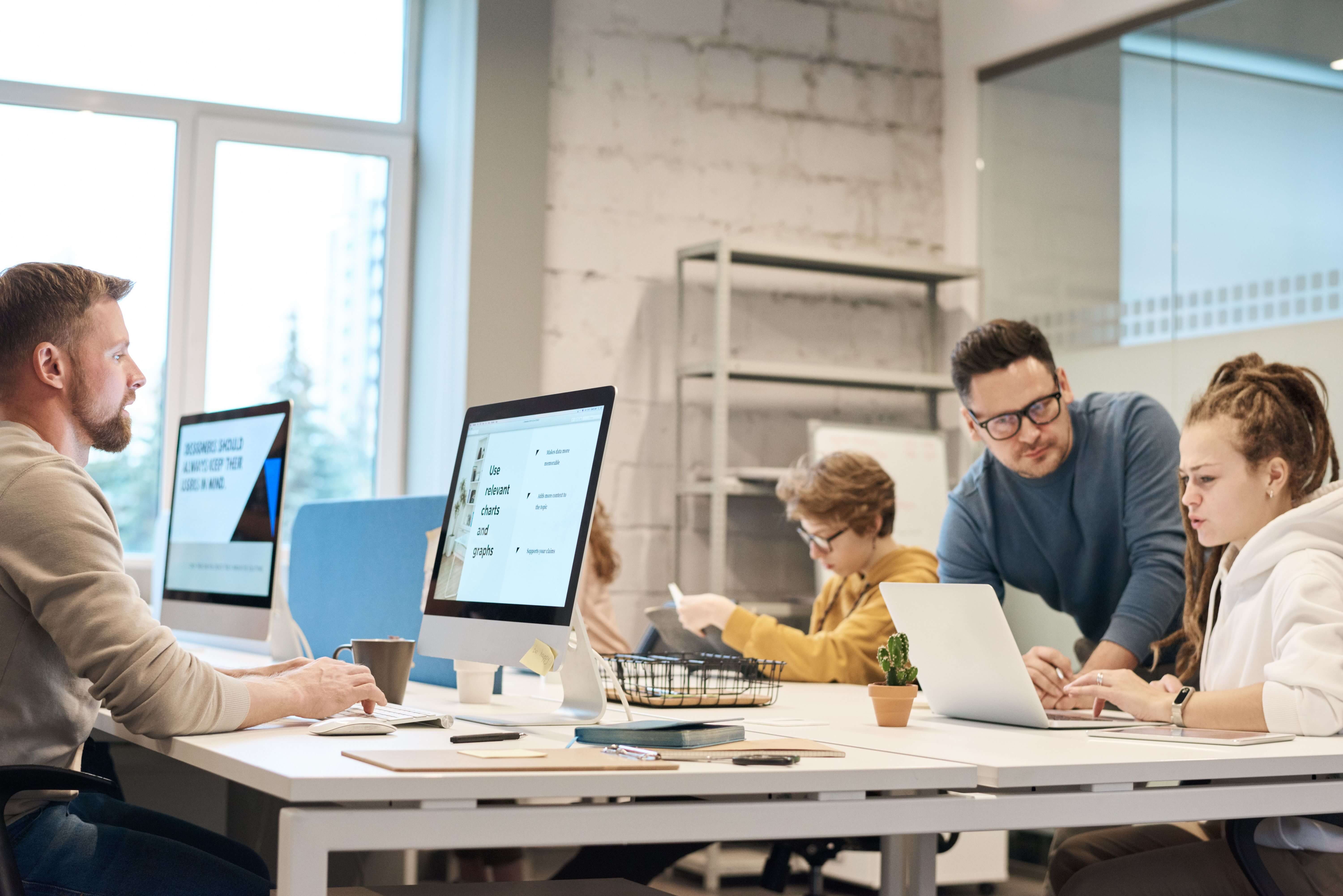 A team reviewing charts and graphs on screen while working together at a row of desks