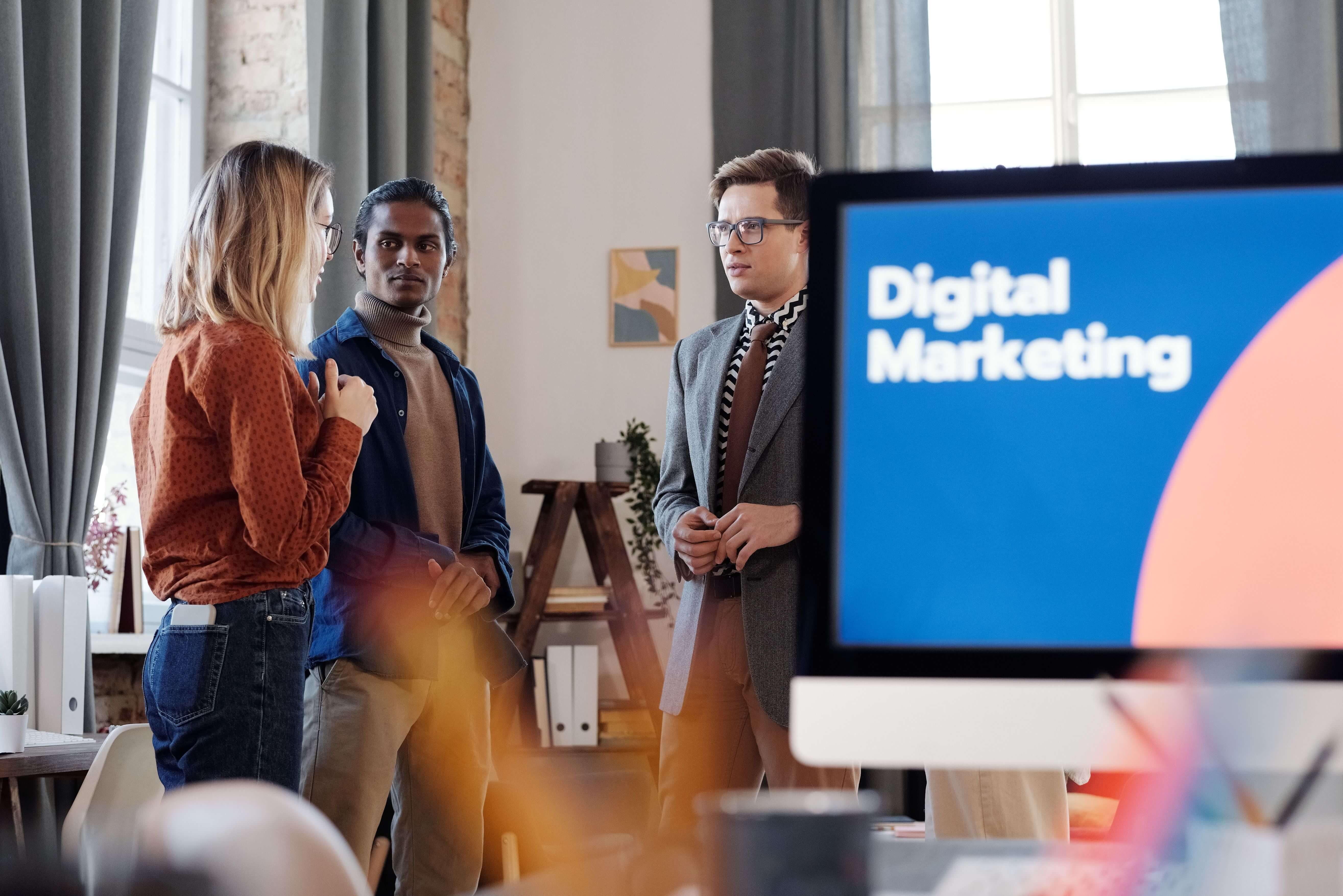 Three colleagues discussing a digital marketing plan beside a presentation screen