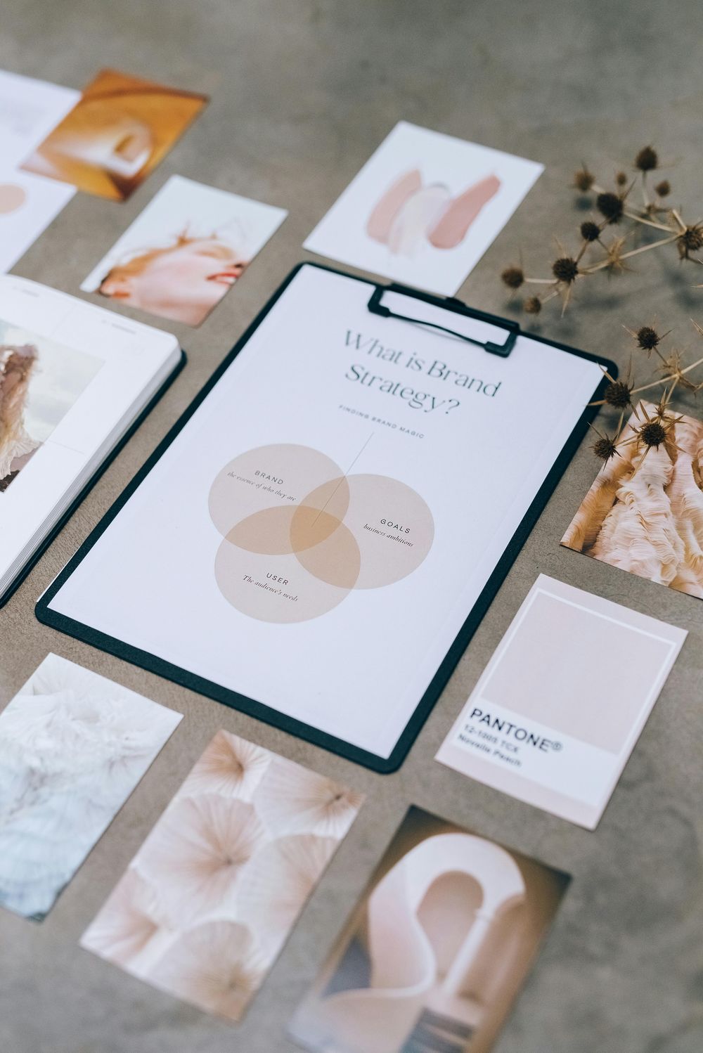 Brand strategy and design work laid out on a desk, including a Pantone chip, a moodboard, and a printed brand strategy diagram